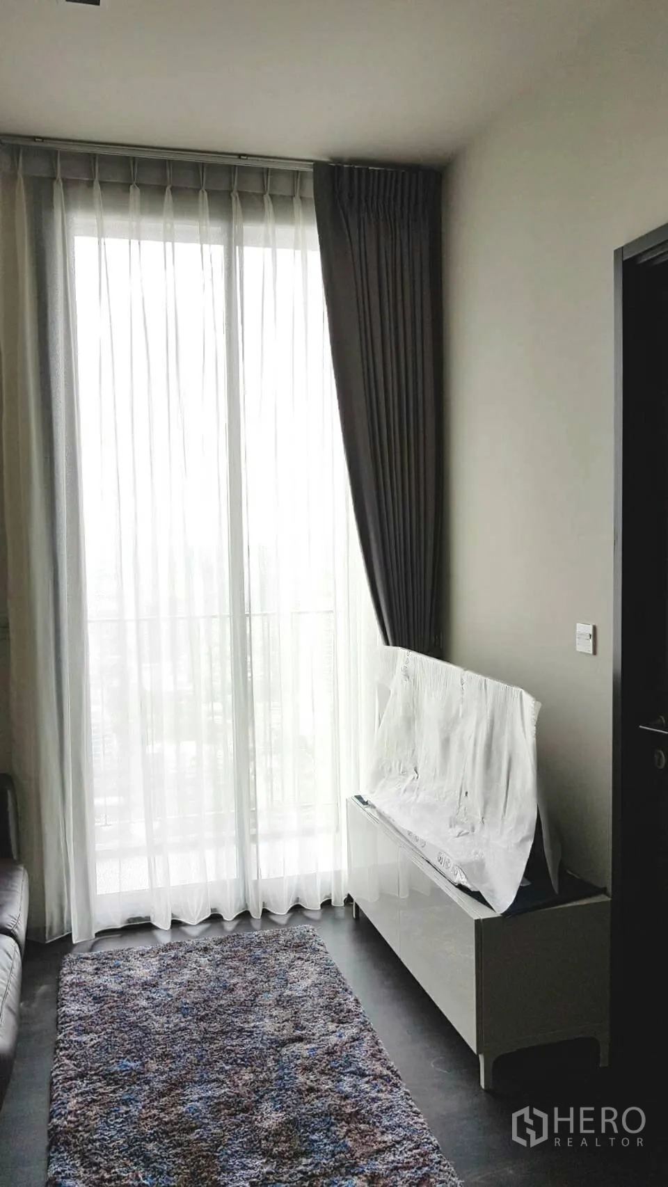 Condominium for rent in Watthana, Bangkok - Living area with large sliding glass doors, layered curtains and a low TV console.