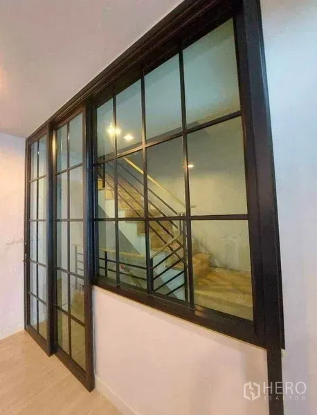 Townhouse for rent in Bang Phli, Samut Prakan - Black-framed sliding glass partition beside the staircase in a bright hallway.