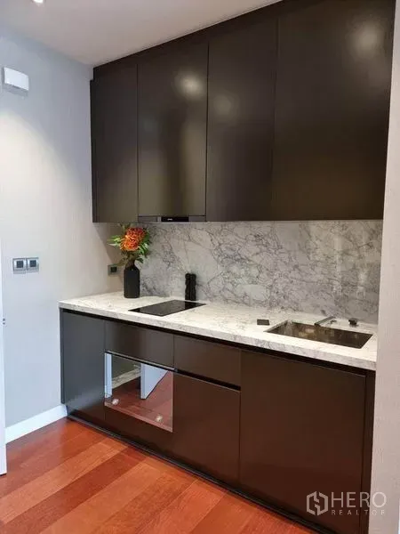 公寓 出租在Watthana, Bangkok - 现代一字型厨房，深色柜体、大理石背板、石材台面、电磁炉与水槽。