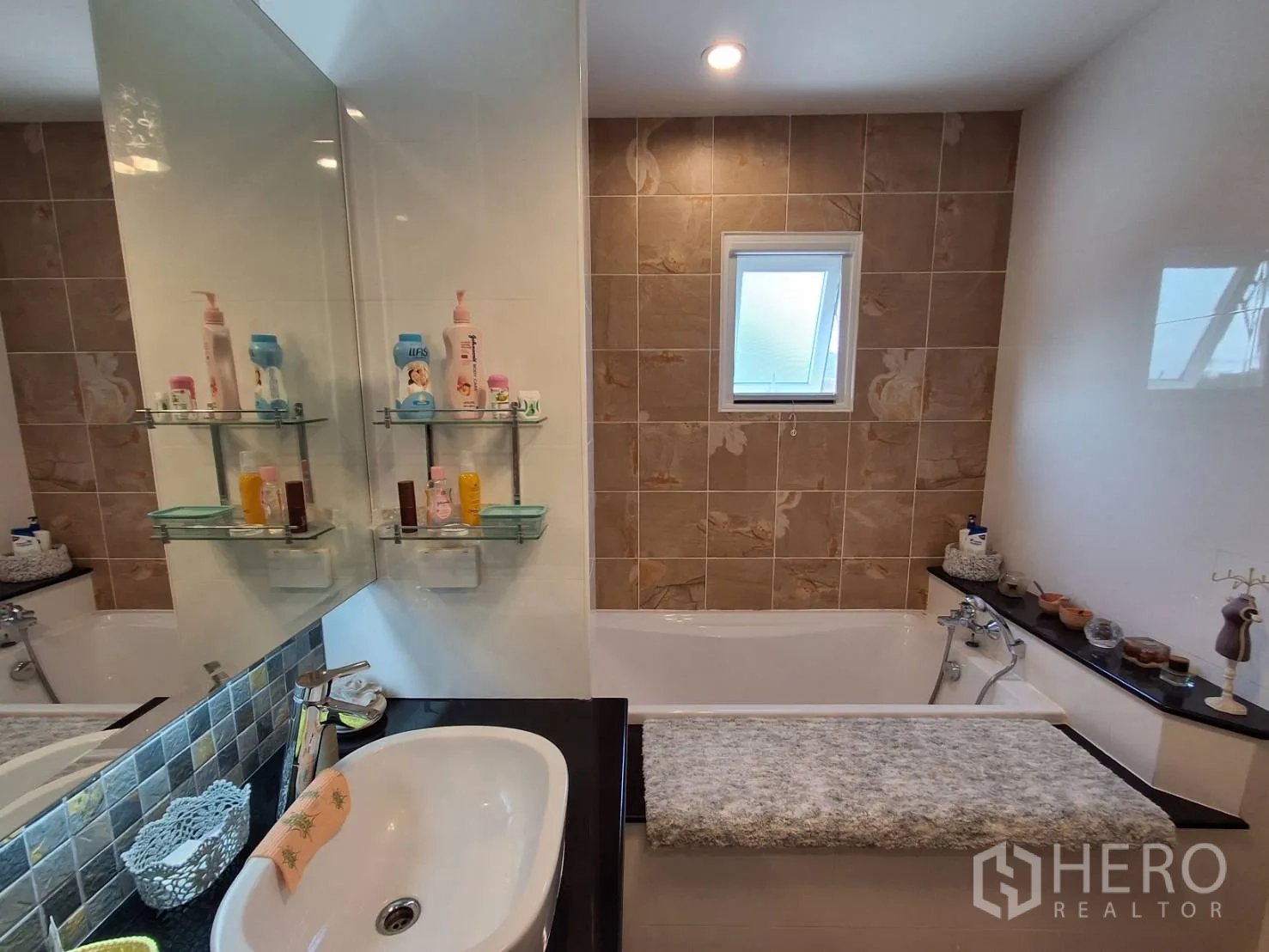 Detached House for rent or sale in Ban Chang, Rayong - Bathroom with large mirror, shelves and bathtub with tiled feature wall.