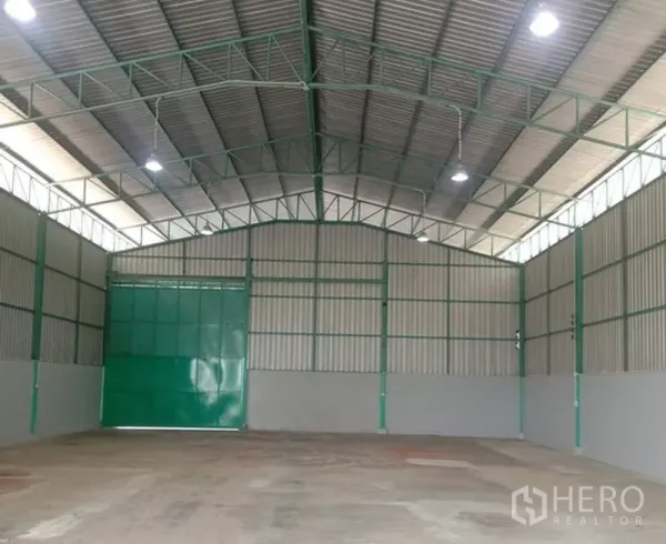 Warehouse for rent in Bang Bua Thong, Nonthaburi - Open storage area with large green sliding door, lit by bright high-bay lights.