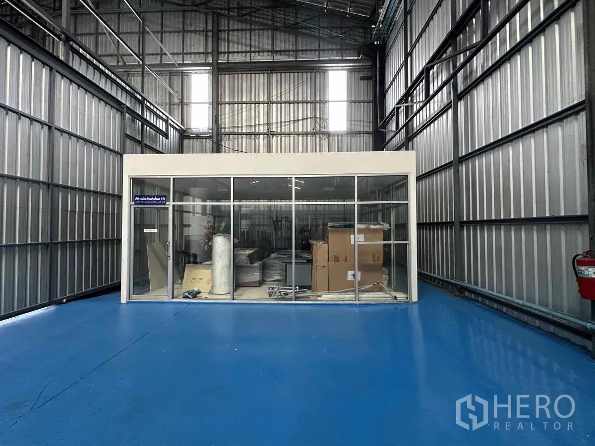 Warehouse for rent in Pak Kret, Nonthaburi - High-bay warehouse space with blue floor and an enclosed glass office cube.