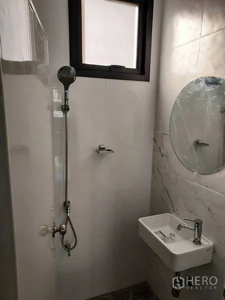 Shophouse for rent in Bang Kapi, Bangkok - Compact bathroom with shower, round mirror, and wall-mounted sink.