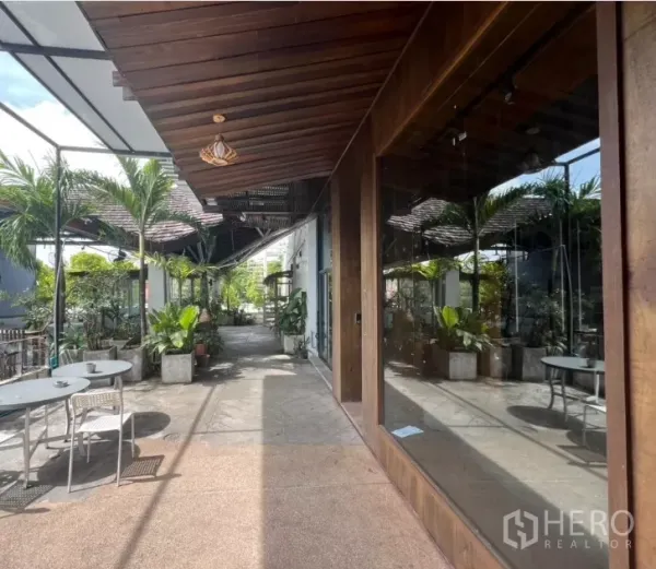 พื้นที่ขายปลีก ให้เช่า - ทางเดินมีหลังคาพร้อมกระถางต้นไม้และโต๊ะคาเฟ่ ขนาบกระจกโชว์เต็มบาน