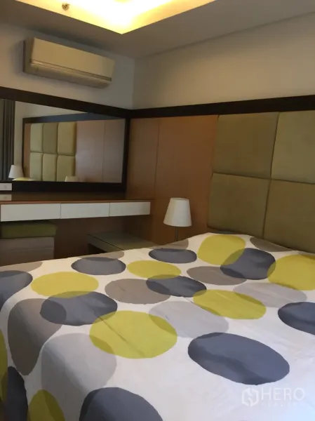 Condominium for rent in Watthana, Bangkok - Bedroom with padded headboard, large wall mirror and built-in vanity.