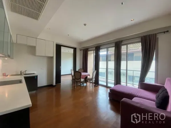 Condominium for rent in Yan Nawa, Bangkok - Bright open-plan living area with wood floors, purple sofa, dining set, and floor-to-ceiling windows to the balcony.