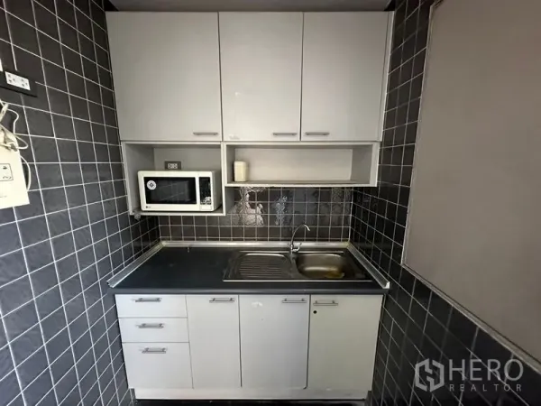 办公空间 出租 - 紧凑茶水间，内置柜体、水槽、台面与微波炉，深色瓷砖墙面。