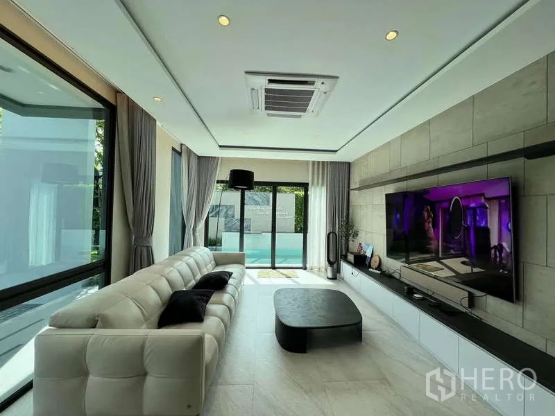 Detached House for rent or sale in Bang Kapi, Bangkok - Family room facing the pool with sofa, large TV wall and full-height windows.