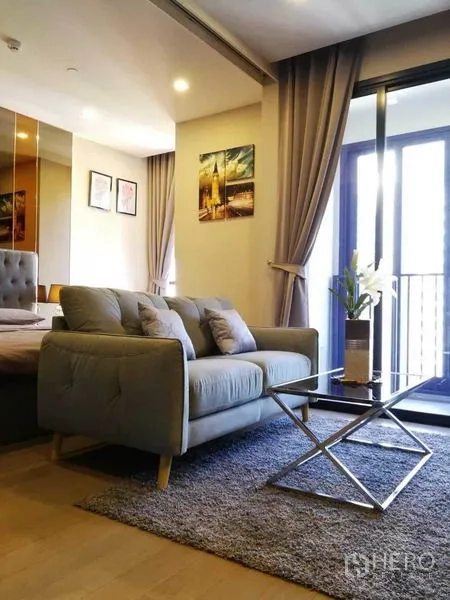 คอนโด ให้เช่าในWatthana, Bangkok - ห้องนั่งเล่นสว่าง โซฟาสีเทา โต๊ะกลางกระจก พรม และประตูกระจกเปิดสู่ระเบียง