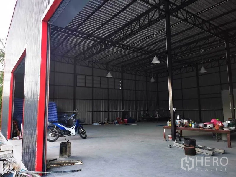 Warehouse for rent - Open-plan warehouse interior seen from a red-framed bay, with steel trusses, high ceiling and a concrete floor.
