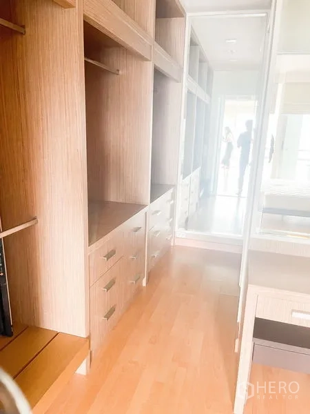 Condominium for rent in Khlong Luang, Pathum Thani - Walk-in closet lined with wood cabinetry, drawers, open shelves, and a mirrored door.