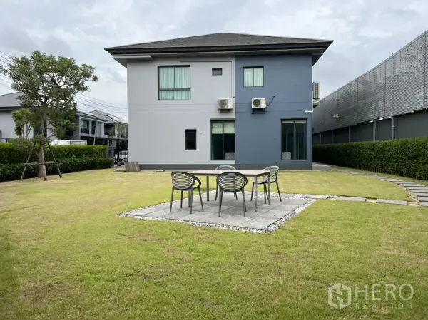 Detached House for rent in Bang Kapi, Bangkok - Expansive back lawn with patio seating, hedges, and the home’s rear façade.