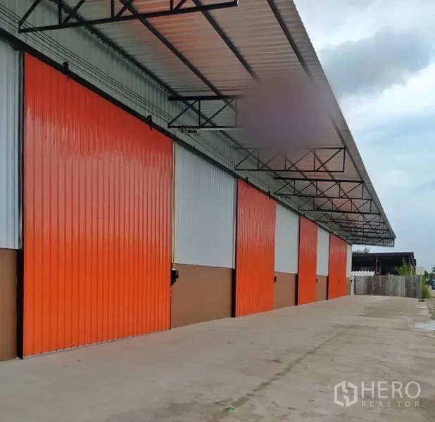 คลังสินค้า ให้เช่าในKhlong Luang, Pathum Thani - แถวโกดังสมัยใหม่ ประตูสไลด์สีส้ม ทางคอนกรีตกว้าง พร้อมหลังคาคลุมลานขนถ่ายสินค้า