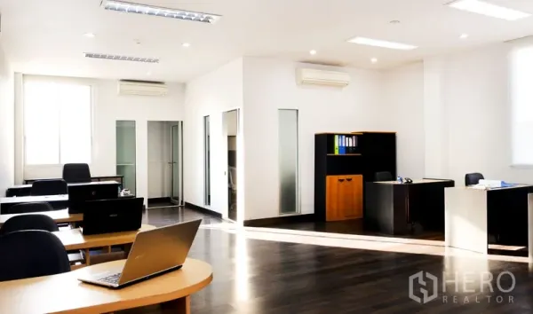 Office Space for rent in Khlong Toei, Bangkok - Spacious office room with multiple workstations, large windows, dark wood floors and split air conditioning.