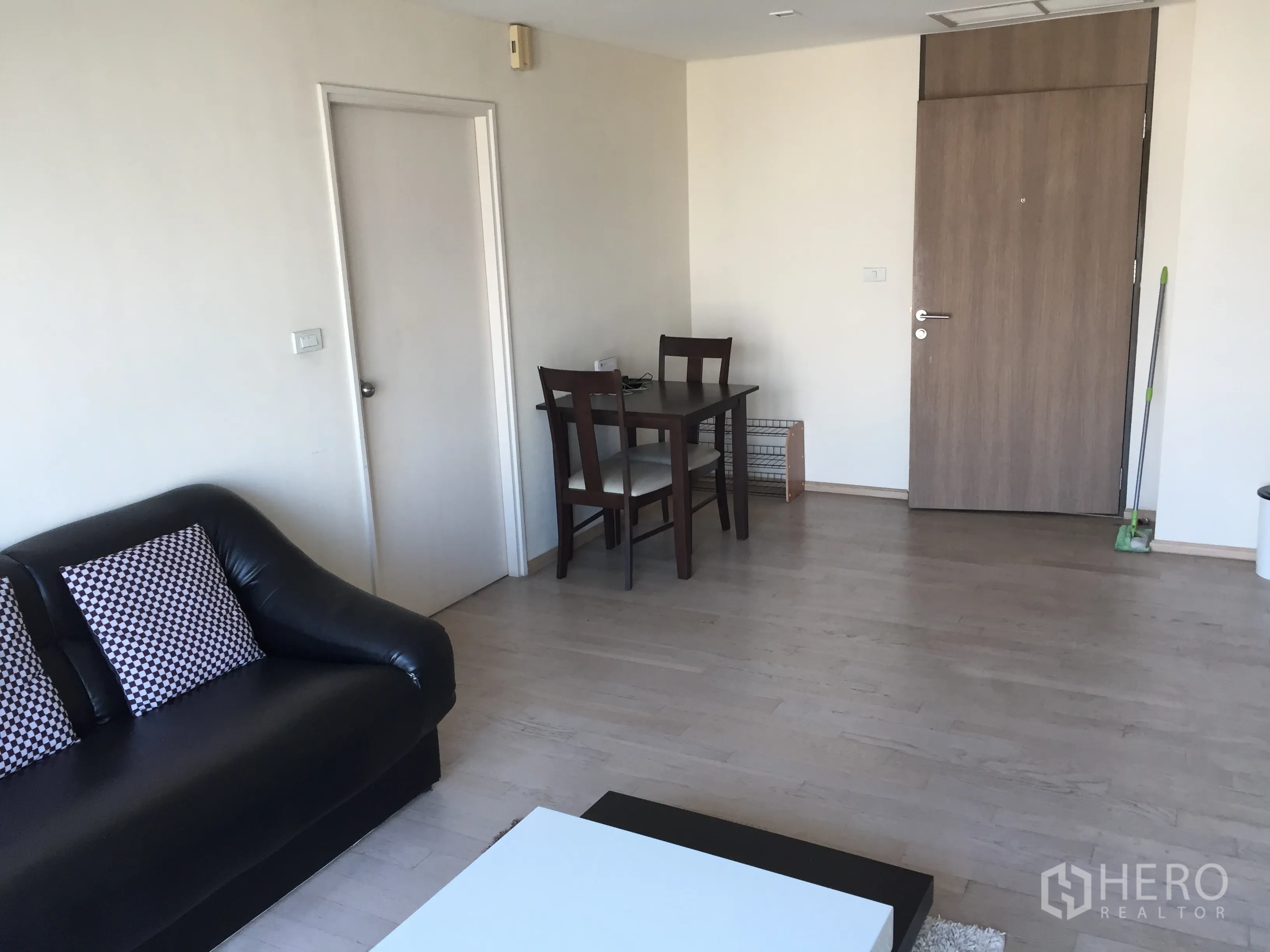 公寓 出租或出售在Khlong Toei, Bangkok - 宽敞起居区，黑色皮沙发与双人餐桌靠近入户门。