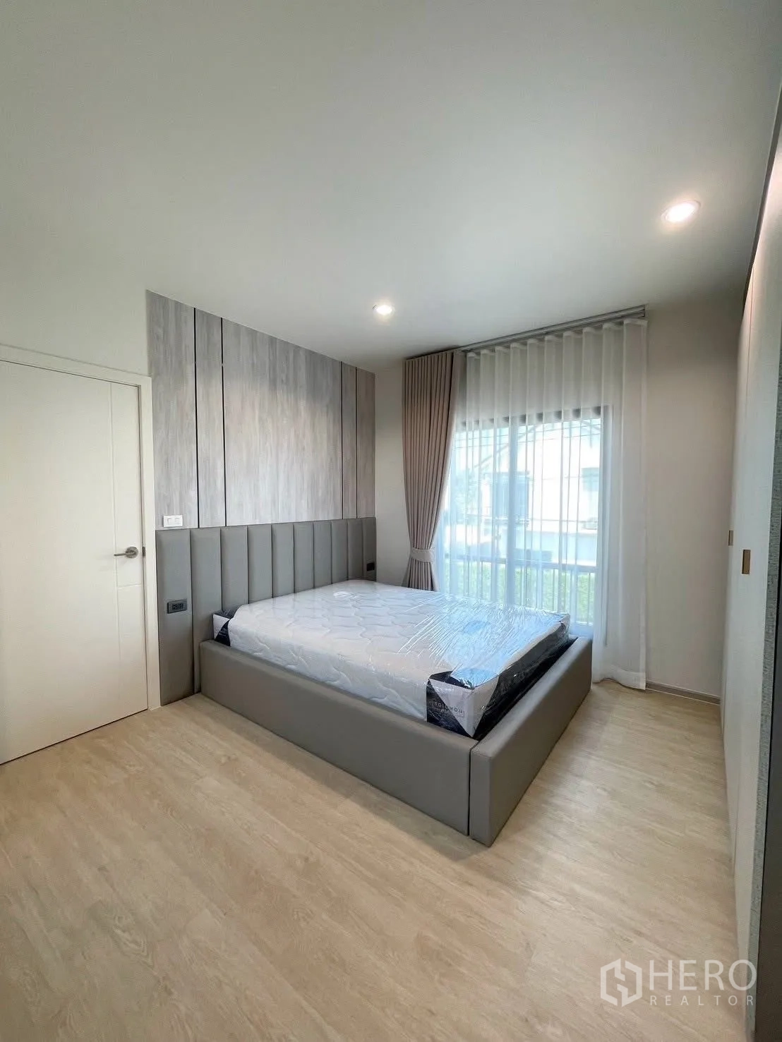 Detached House for rent in Bang Phli, Samut Prakan - Guest bedroom with gray upholstered bed and headboard, floor-to-ceiling window and neutral decor.