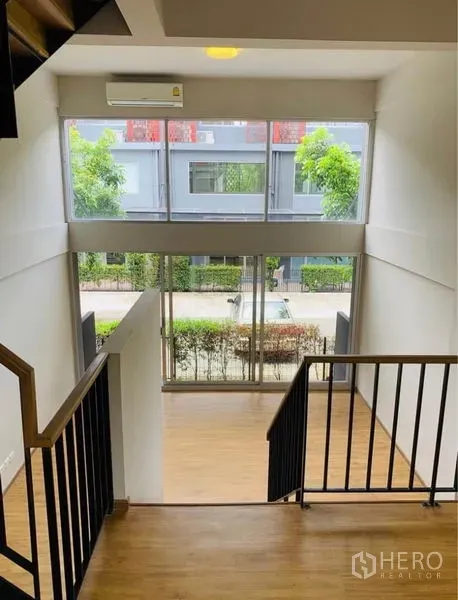 Home Office for rent - View from staircase to front lounge with tall glazing and green streetscape outside.