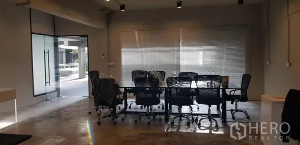 Office Space for rent in Khlong Toei, Bangkok - Conference area with long meeting table, mesh chairs, glass entrance and window blinds letting in natural light.