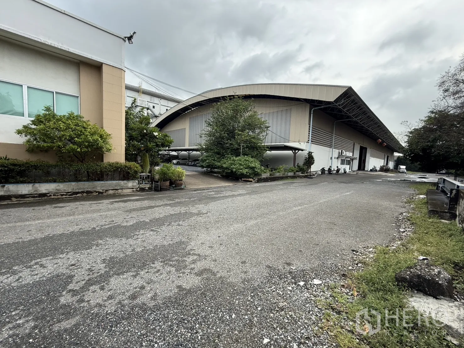 Factory for rent in Bang Phli, Samut Prakan - Curved-roof warehouse next to landscaped planters and a broad driveway.