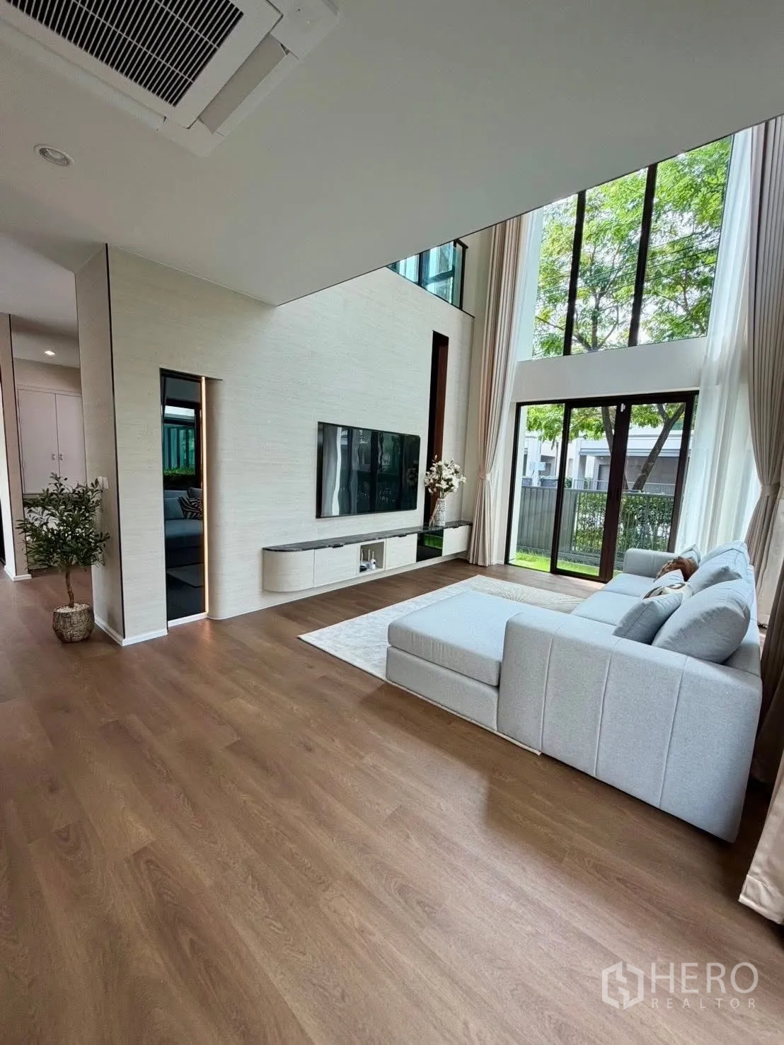 Detached House for rent in Bang Phli, Samut Prakan - Spacious living room with TV wall, L-shaped sofa and tall glass windows facing the yard.