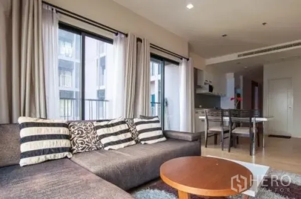 คอนโด ให้เช่าหรือขายในWatthana, Bangkok - โซนนั่งเล่นแบบโอเพ่นพร้อมโซฟาตัวแอล โต๊ะกลาง และหน้าต่างสูงจรดเพดานมองเห็นคอร์ทยาร์ด