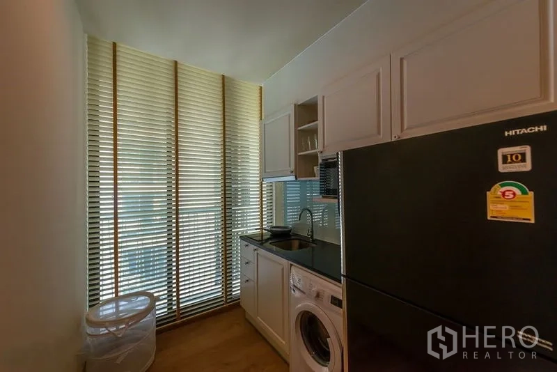 Condominium for rent in Watthana, Bangkok - Kitchenette with sink, washer and tall fridge, framed by full-height vertical blinds.