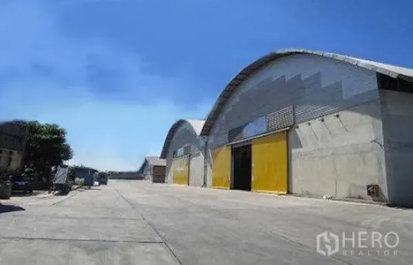 Warehouse for rent in Phra Pradaeng, Samut Prakan - Row of warehouses with yellow doors and broad driveway suitable for trailers and containers.