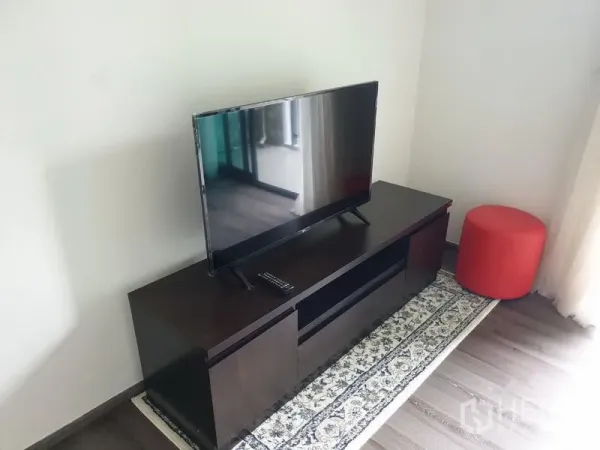 Condominium for rent in Watthana, Bangkok - Flat-screen TV on dark wood cabinet beside a window with sheer curtains.