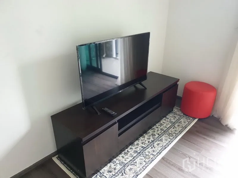 Condominium for rent in Watthana, Bangkok - Flat-screen TV on dark wood cabinet beside a window with sheer curtains.