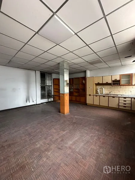 Shophouse for rent in Sathon, Bangkok - Open workspace with kitchenette, tiled backsplash, built-in cupboards, and a central support column.