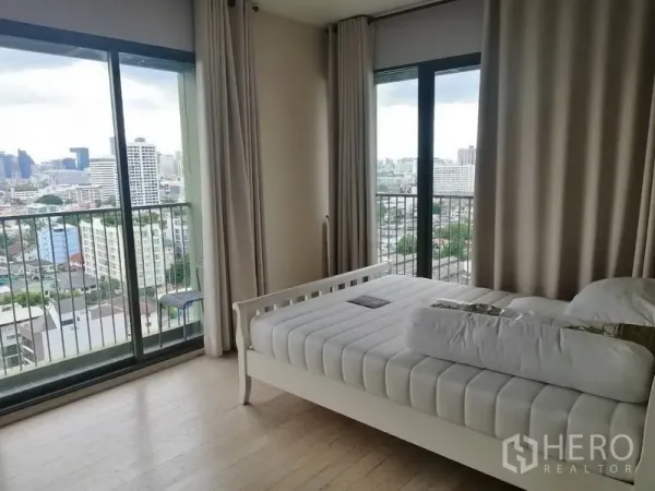 公寓 出租在Watthana, Bangkok - 卧室配白色床架，落地窗与阳台，可欣赏城市天际线景观。