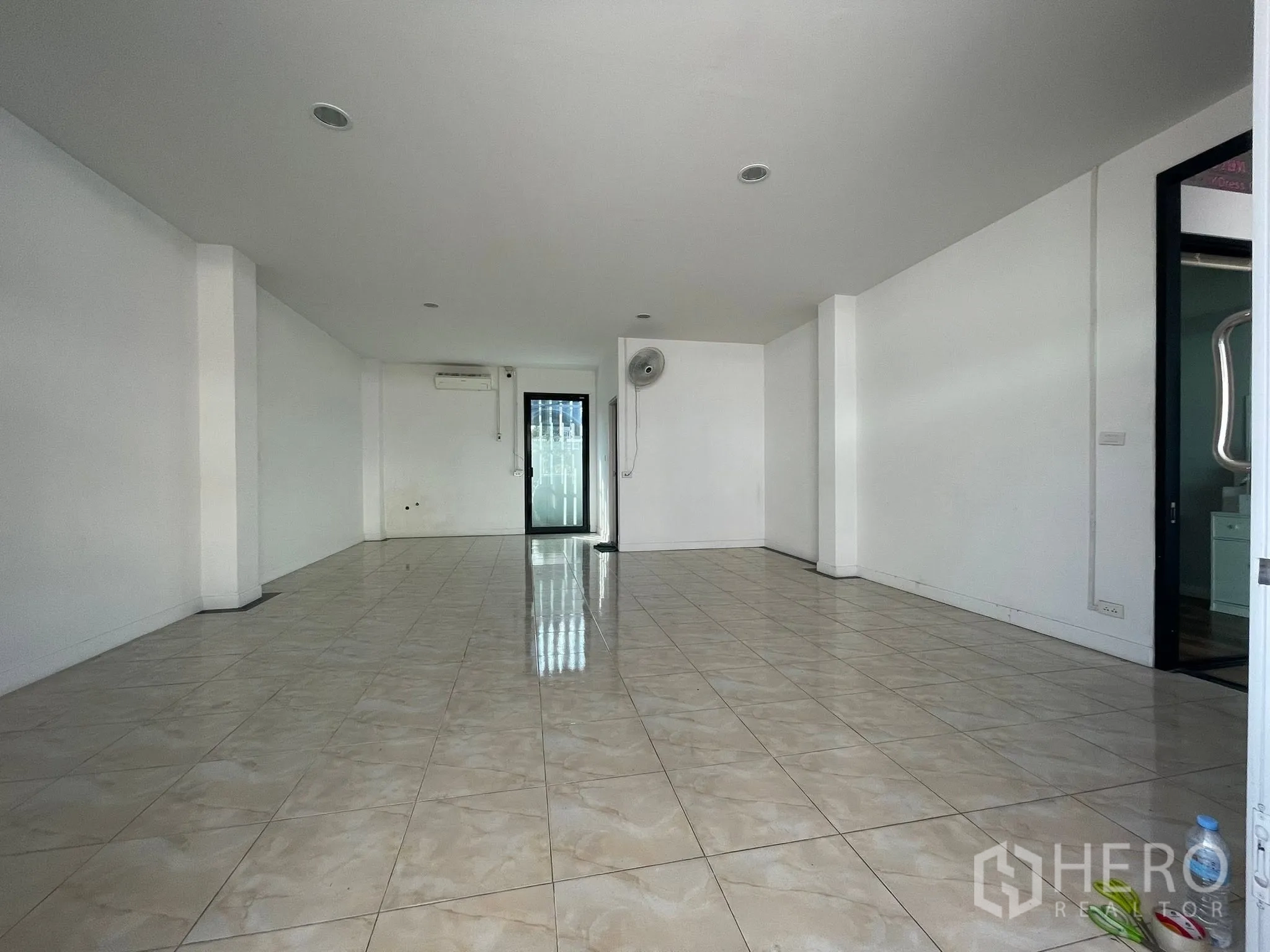 Detached House for rent or sale in Lam Luk Ka, Pathum Thani - Large empty tiled room with a wall fan and rear door.