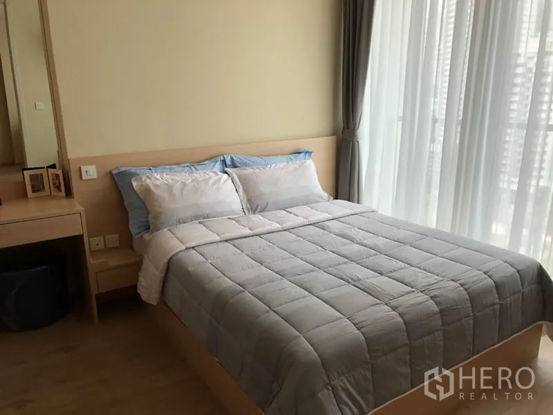 คอนโด ให้เช่าในWatthana, Bangkok - ห้องนอนที่สองเฟอร์นิเจอร์ไม้สีอ่อน มีโต๊ะเครื่องแป้ง และวิวเมืองผ่านผ้าม่านโปร่ง