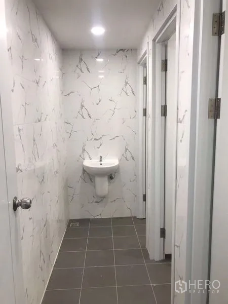 Warehouse for rent or sale in Nong Chok, Bangkok - Corridor of modern restrooms with marble-look tiles, gray floor and a wall-mounted sink.