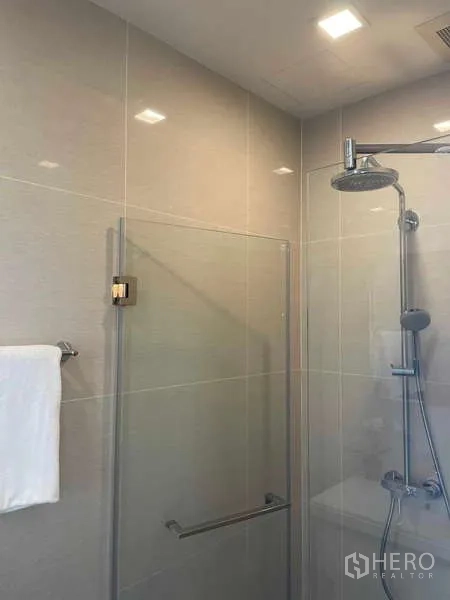 Condominium for rent or sale - Contemporary bathroom with glass-enclosed shower, rainfall showerhead and beige tiled walls.