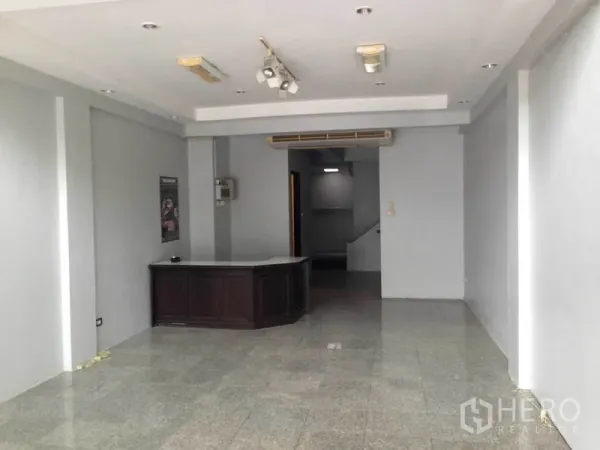 Home Office for rent or sale in Wang Thonglang, Bangkok - Ground-floor open workspace with a reception desk, gray walls, recessed ceiling lights and a rear staircase.
