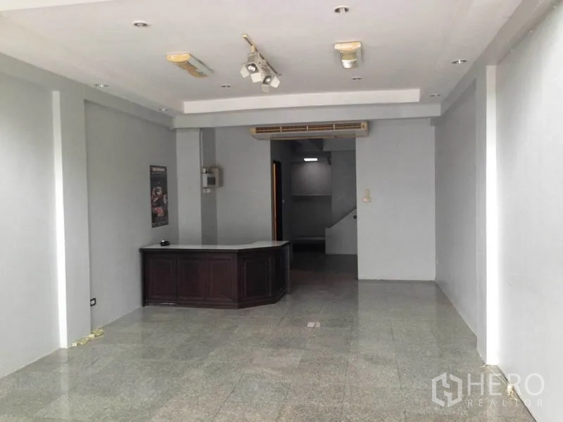 Home Office for rent or sale in Wang Thonglang, Bangkok - Ground-floor open workspace with a reception desk, gray walls, recessed ceiling lights and a rear staircase.