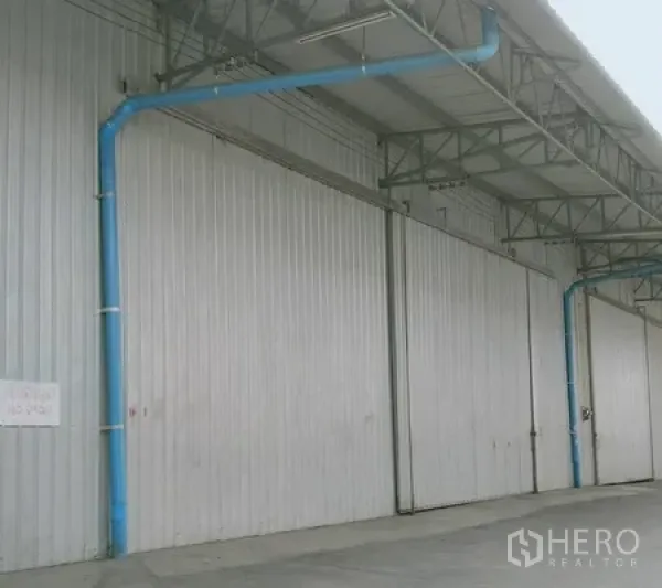 货栈 出租在Khlong Luang, Pathum Thani - 钢结构仓库外立面，超大金属推拉门，带雨棚的装卸区与蓝色管线。