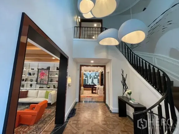 บ้าน ให้เช่าหรือขายในSaphan Sung, Bangkok - โถงรับแขกเพดานสูงสองชั้น บันไดโค้ง โคมไฟดีไซน์ และพื้นปาร์เกต์ เชื่อมสู่พื้นที่นั่งเล่น