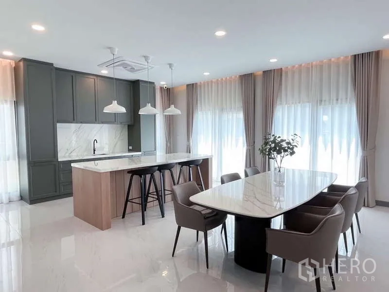 Detached House for rent or sale in Bang Phli, Samut Prakan - Contemporary kitchen with marble island, pendant lights and dining table by full-height curtains.