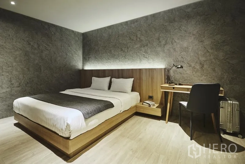 Apartment for rent in Khlong Toei, Bangkok - Bedroom with platform bed, textured feature wall, soft underlit headboard and a wooden work desk.