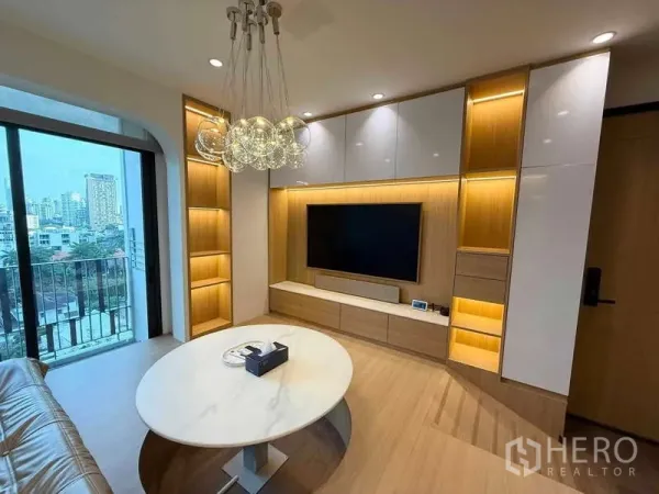Condominium for rent in Watthana, Bangkok - Close view of living area with marble oval coffee table, illuminated shelving, and floor-to-ceiling window to balcony.