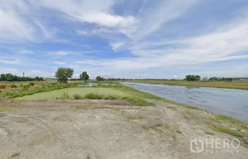 Land for sale in Chachoengsao - Wide view across ponds and a gravel access area on flat open land.