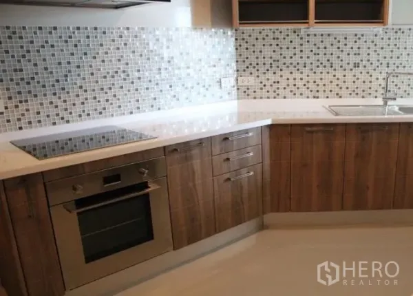 Condominium for rent in Watthana, Bangkok - Modern L-shaped kitchen with wood cabinets, quartz countertop, mosaic tile backsplash, electric cooktop and built-in oven.