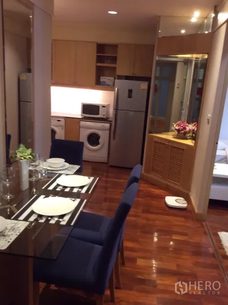 Condominium for rent in Pathum Wan, Bangkok - Dining area with glass table and blue upholstered chairs overlooking the kitchen.