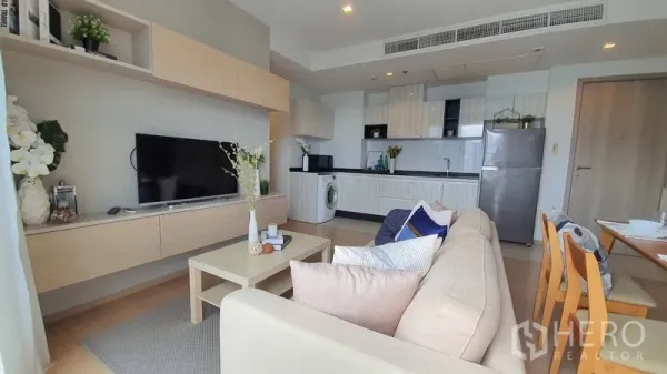 Condominium for rent in Watthana, Bangkok - Bright open-plan living room with sofa, TV and built-in shelving beside a modern kitchen.