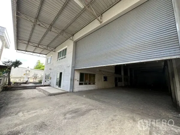 工厂 出租或出售在Bang Bua Thong, Nonthaburi - 带遮雨装卸棚的入口区域，超大卷闸门与两层办公立面。