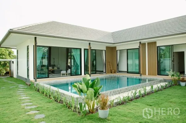 独立式住宅 出售在Phra Pradaeng, Samut Prakan - L形当代住宅环绕铺砖泳池，草坪与景观植物相映