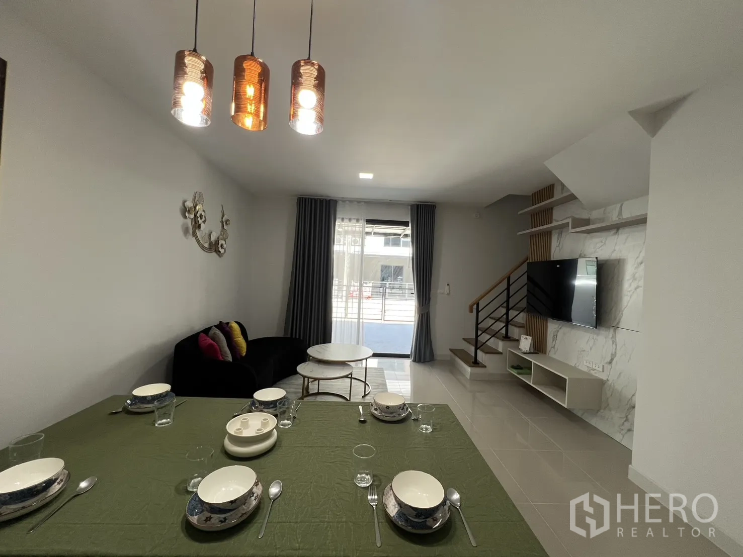 Townhouse for rent in Bang Phli, Samut Prakan - Dining area set for meals with sofa and TV opposite a marble feature wall.
