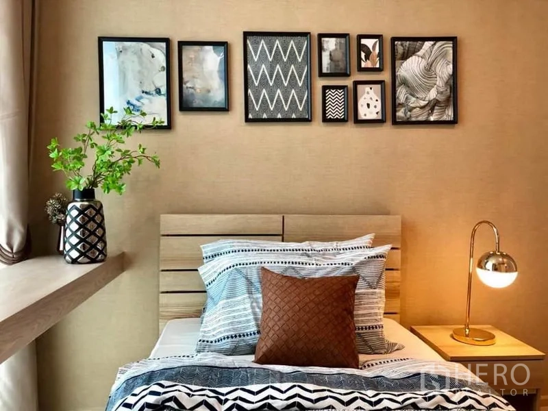 Condominium for rent or sale in Huai Khwang, Bangkok - Cozy bedroom with single bed, gallery wall artwork, bedside lamp, and window ledge with a plant.